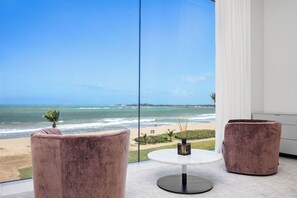 A room with a large window overlooking a beach, two plush chairs, a small table, and a white cabinet. - Amazing Four Seasons Beachfront 4BR Residence - Golf Cart Included (Río Grande)