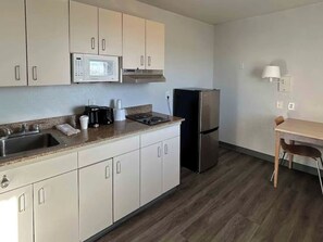 Una cocina con armarios blancos, microondas, estufa, refrigerador, lavaplatos y una mesa con sillas.