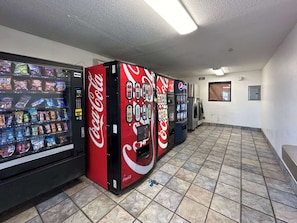 Una hilera de máquinas expendedoras con la marca Coca-Cola, un suelo de baldosas y una pared lisa con una puerta.