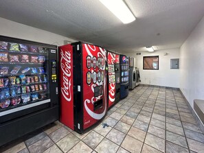 Fila de màquines expenedores amb el logotip de Coca-Cola, un sòl de rajoles i una paret sense decoració amb una porta.