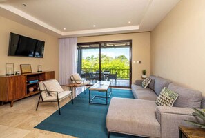 A modern living room with a sofa, armchair, coffee table, and a flat-screen TV mounted on the wall. - Condo in Playa Ocotal | Sunset Terrace & Pool (Playa Ocotal)