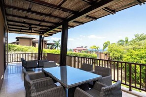 Eine Terrasse im Freien mit Tisch und Stühlen, ein überdachter Bereich mit Dach und ein Blick auf Grünflächen und Gebäude im Hintergrund.