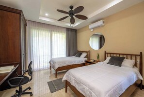 A hotel room with two beds, a desk, a chair, a ceiling fan, and an air conditioning unit. - Condo in Playa Ocotal | Sunset Terrace & Pool (Playa Ocotal)