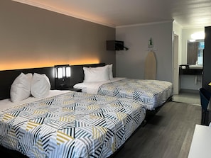 Ein Hotelzimmer mit zwei Betten, einem Nachttisch, einem an der Wand befestigten Fernseher und einem durch eine offene Tür erreichbaren Badezimmer.