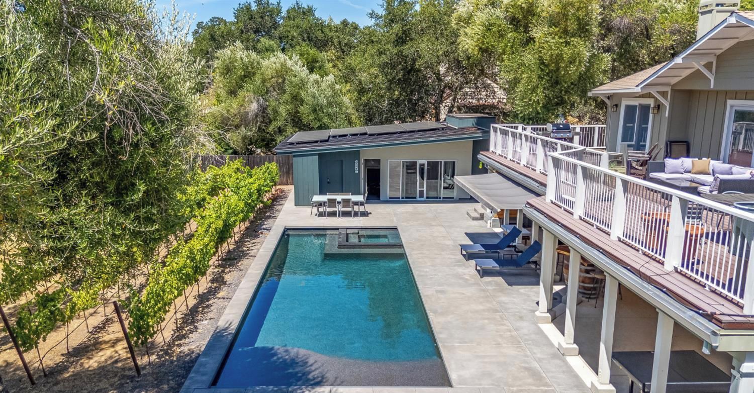 A rectangular swimming pool with a deck, surrounded by a wooden fence and trees.