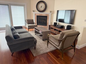 Un salon comprenant un canapé, un fauteuil, une table basse, une cheminée, un téléviseur et un plancher en bois.
