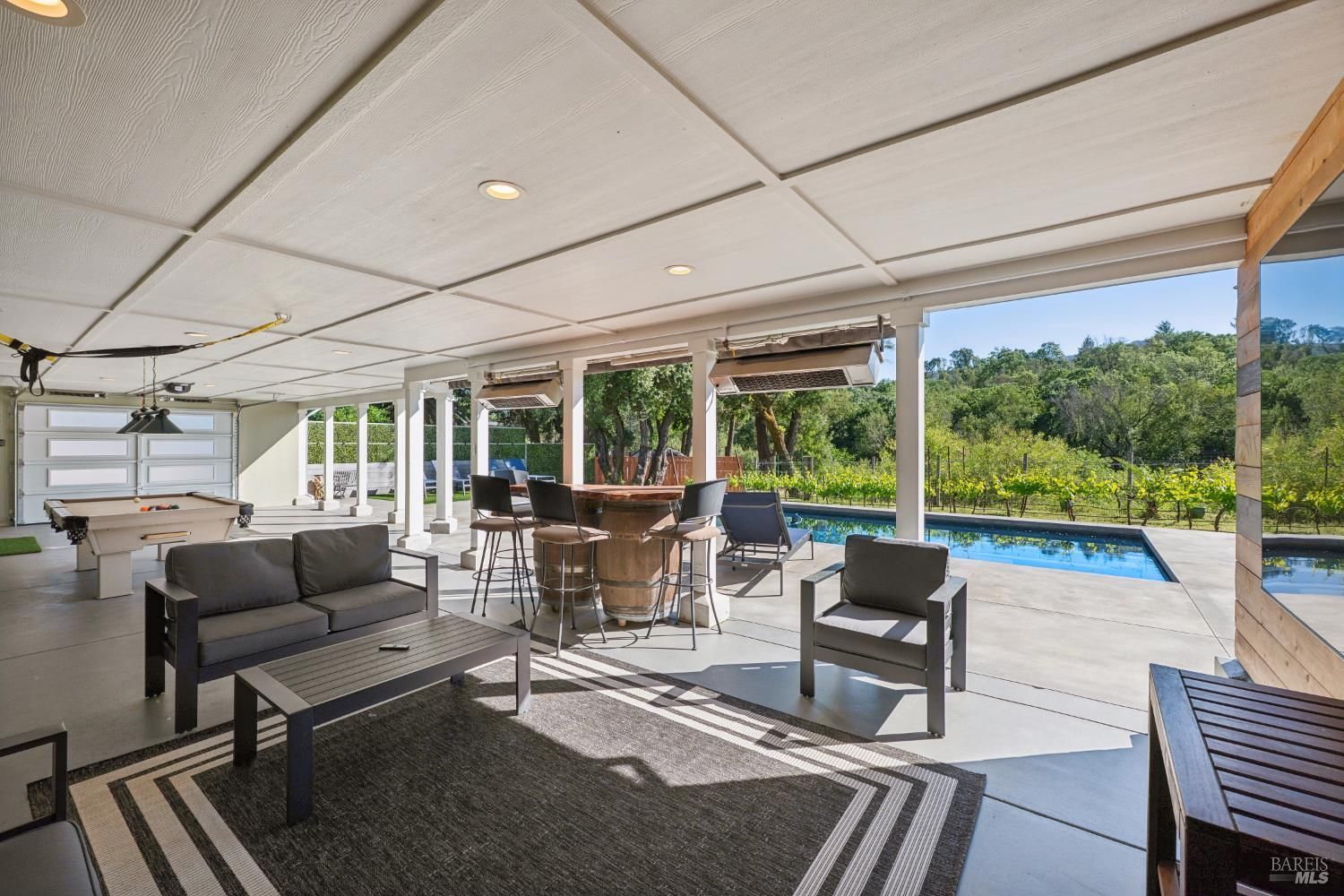 A modern outdoor living space with a pool, seating area, and a view of a vineyard.