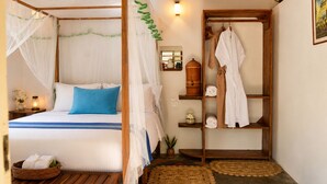 Quarto com cama de dossel, prateleira de madeira com toalhas e mesa de cabeceira com abajur.