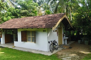A small, single-story building with a tiled roof, a bicycle parked outside, and a well-maintained lawn.