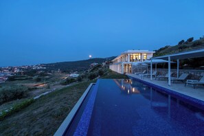 A swimming pool with a view of a hillside and a building with outdoor seating.