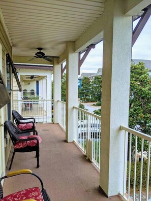 A covered porch with a ceiling fan, two wicker chairs with cushions, and a view of a residential street. - Luna Del Mar - Beach Oasis Home - Pool/Relax/Grill (Destin)