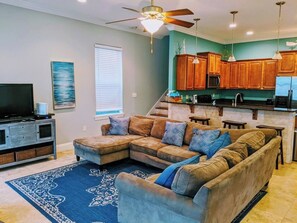 A living room with a sectional sofa, a flat-screen TV, and a blue patterned rug. - Luna Del Mar - Beach Oasis Home - Pool/Relax/Grill (Destin)