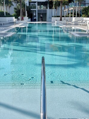 A clear swimming pool with a metal handrail in the foreground, surrounded by lounge chairs and palm trees. - Luxury 2BR Retreat in Flagler Village / Private Terrace + King Bed (Fort Lauderdale)