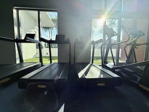 Un gimnasio con cintas de correr y equipo de ejercicio, ventanas amplias y vistas al exterior.