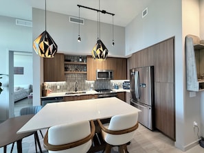 Una cocina moderna con una isla central, electrodomésticos de acero inoxidable e iluminación colgante.