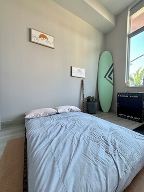 Une chambre avec un lit, une planche de surf et deux tableaux encadrés accrochés au mur.