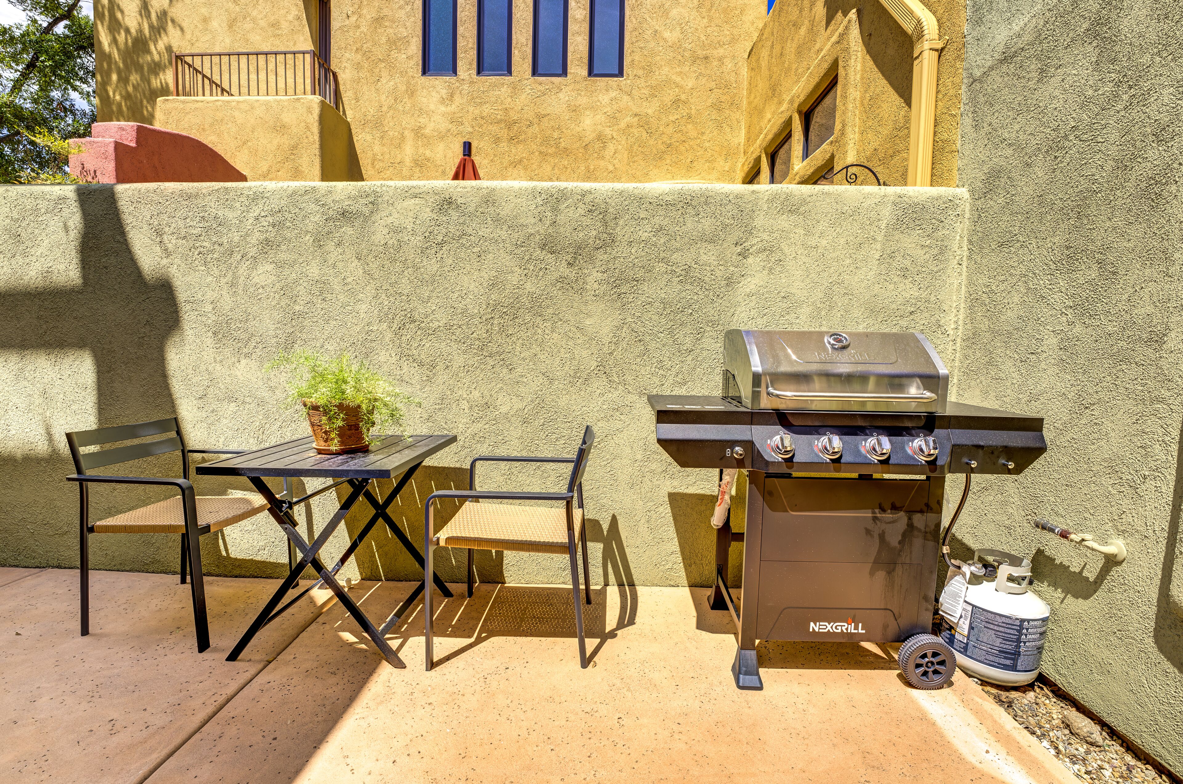Un patio al aire libre con una parrilla, dos sillas y una mesa pequeña.