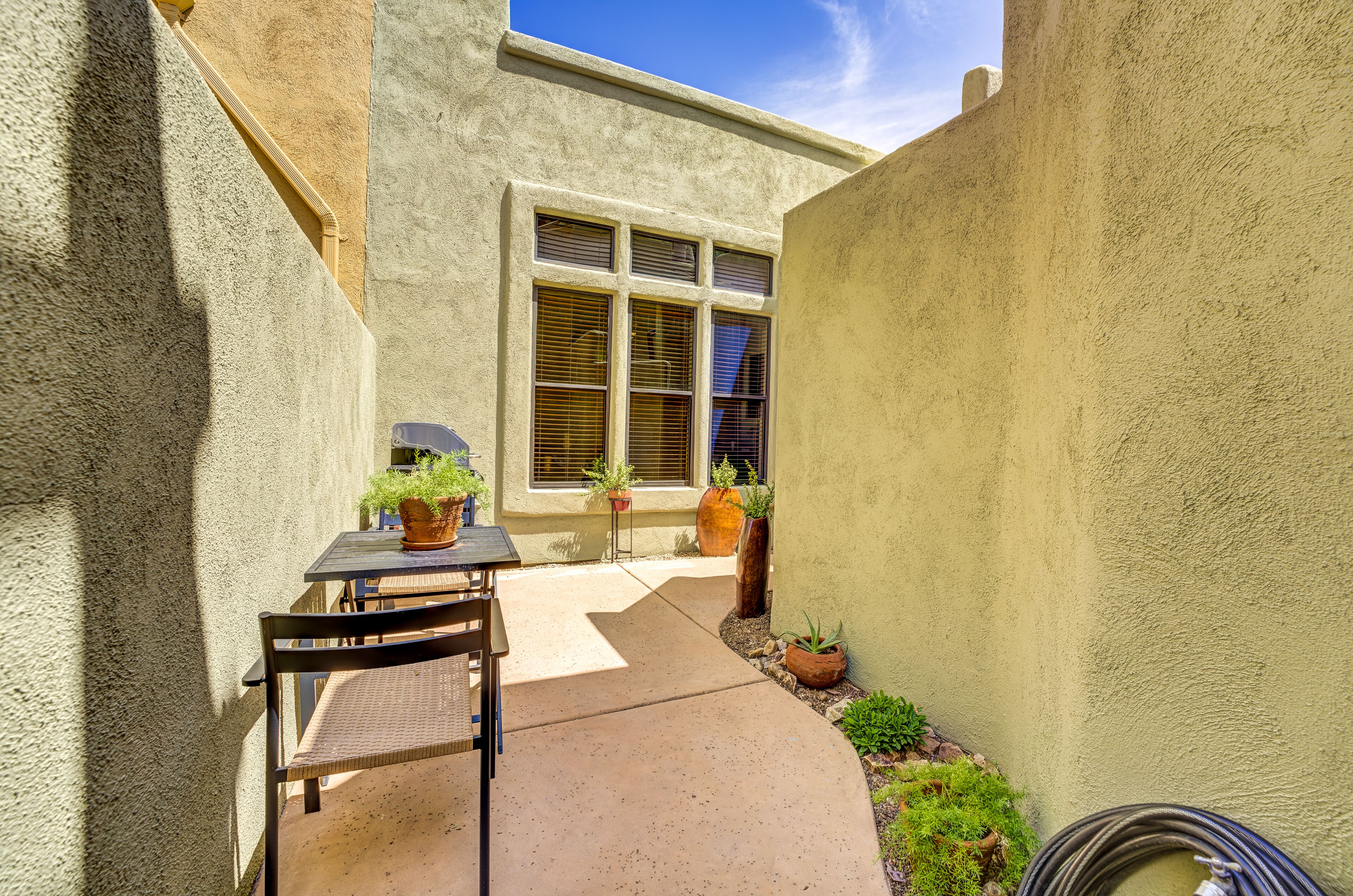 A patio area with a table and chairs, potted plants, and a window with blinds.