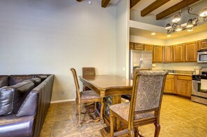 A modern kitchen with wooden cabinets, stainless steel appliances, and a dining area with a leather couch and ornate chairs.