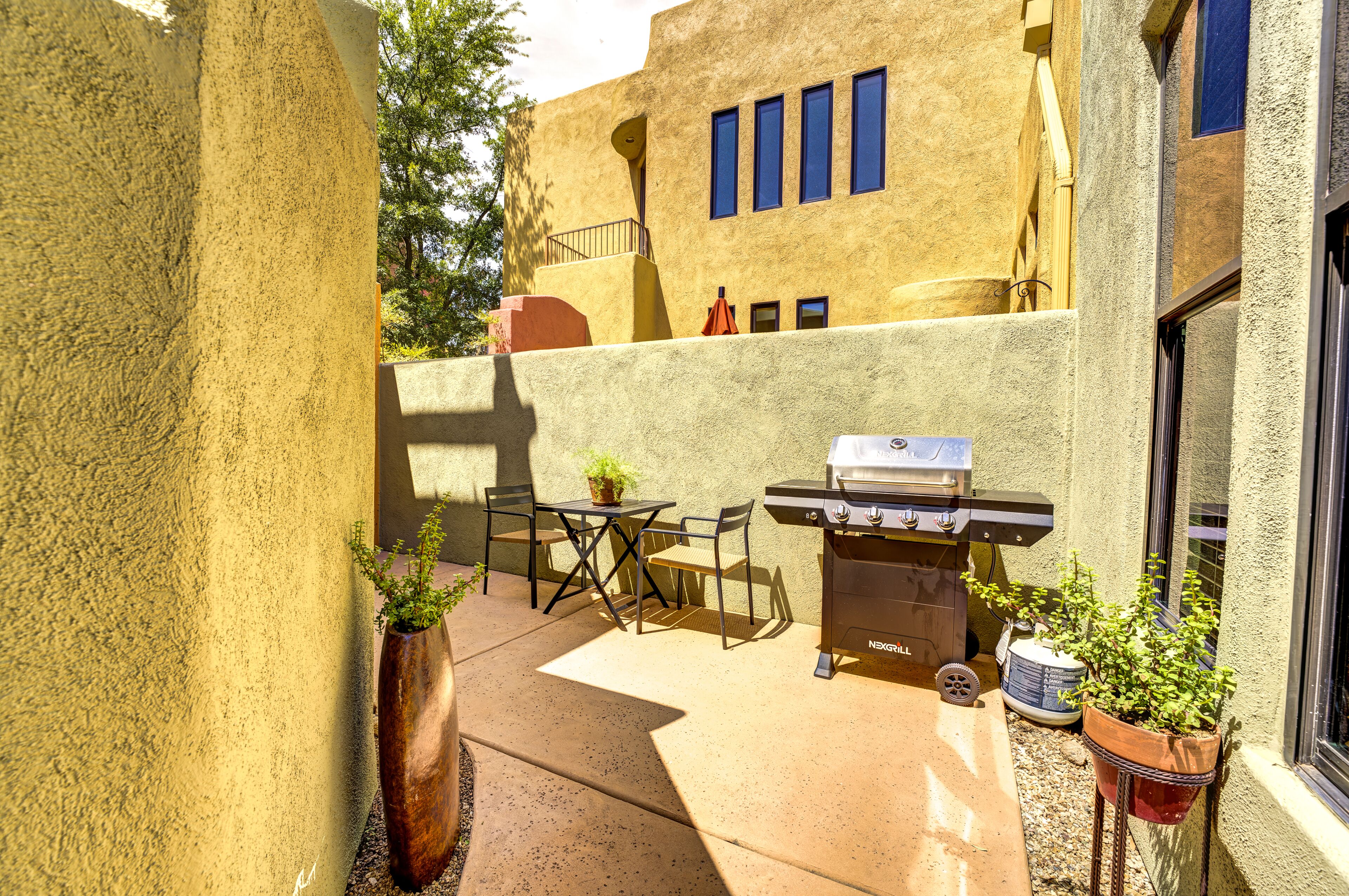 An outdoor patio with a grill, a table, chairs, and potted plants.
