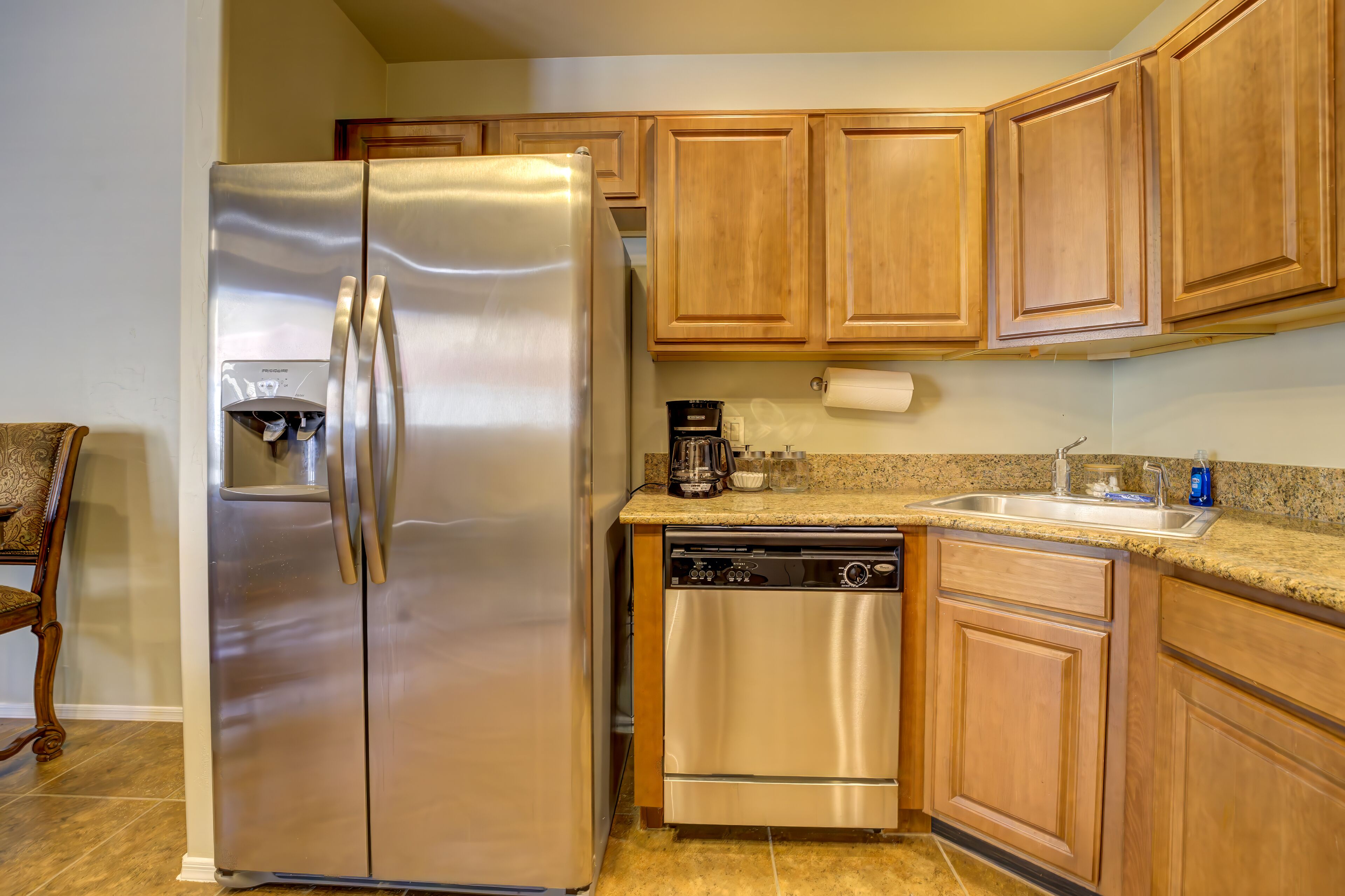A kitchen with a stainless steel refrigerator, a dishwasher, wooden cabinets, and a granite countertop.
