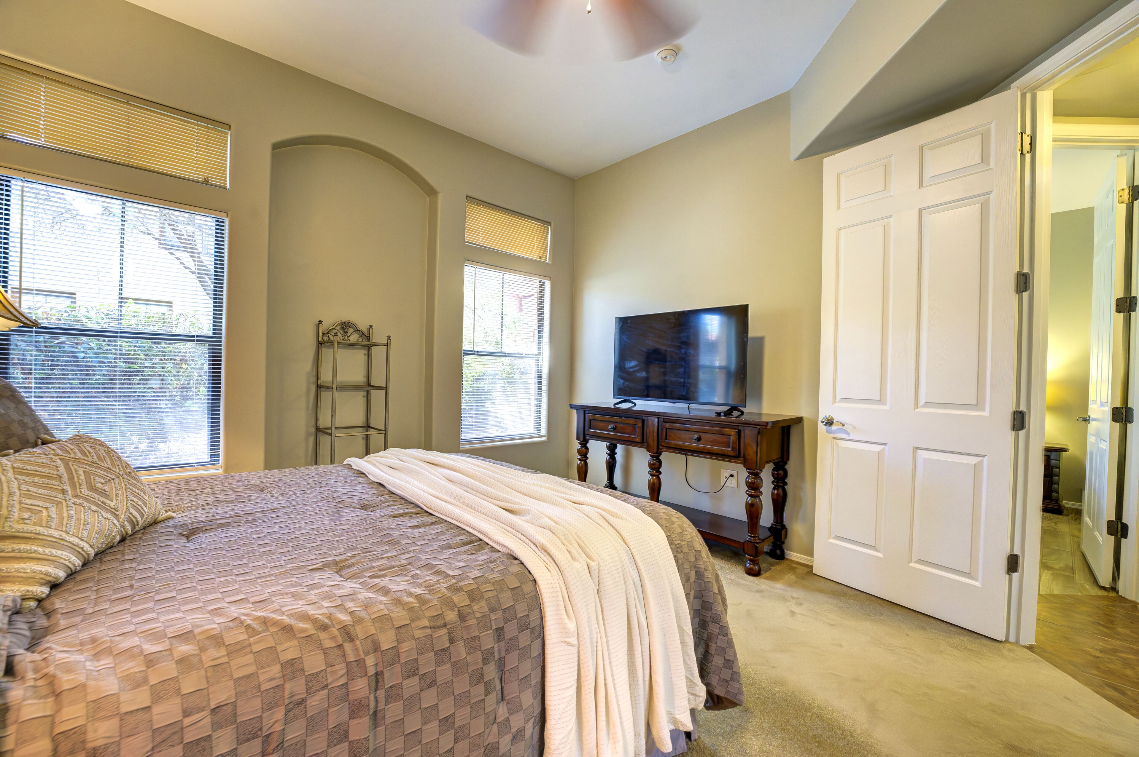 A bedroom with a bed, a dresser, a television, and a door leading to another room.