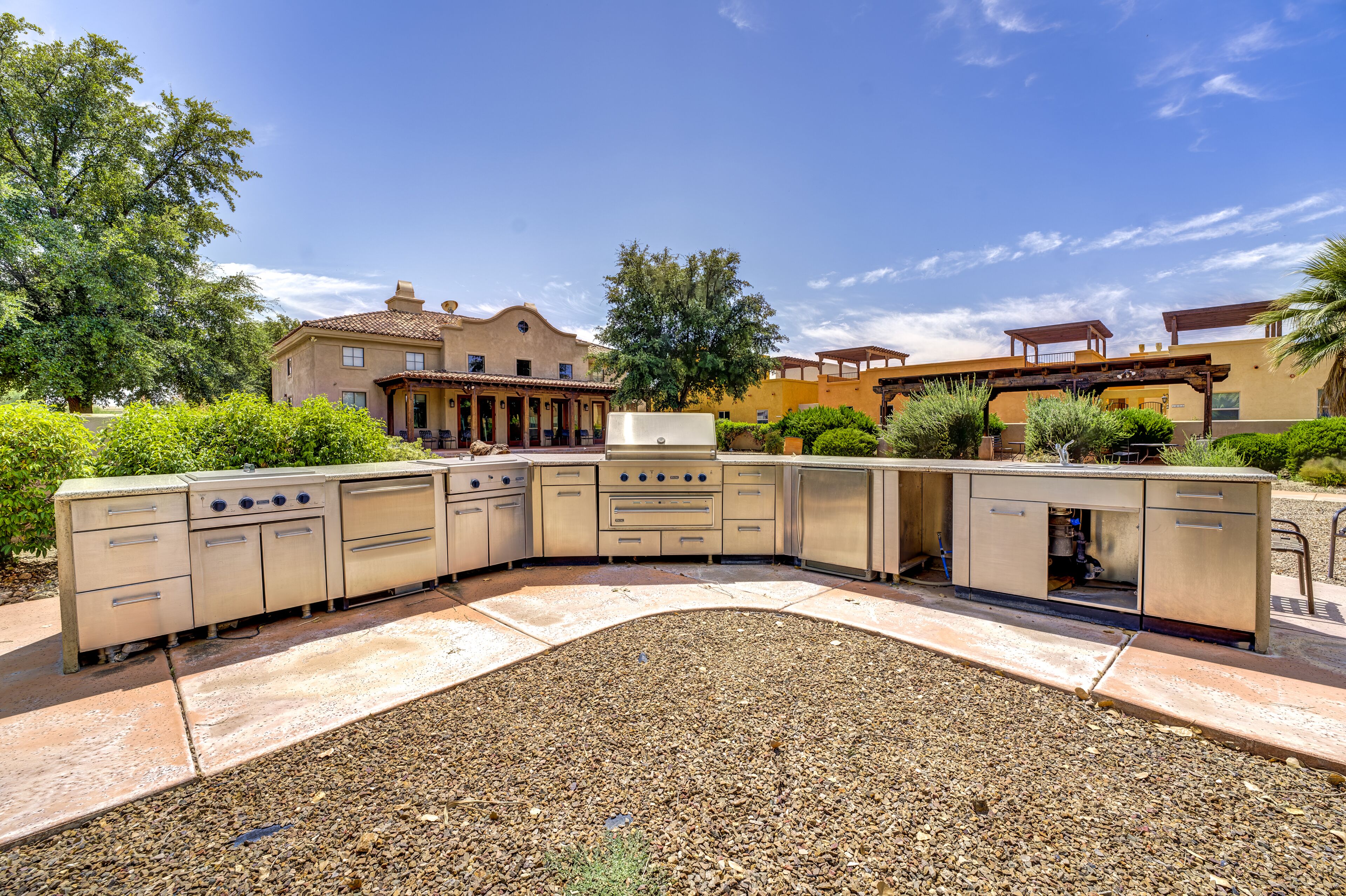 Un patio con una zona de cocina integrada, una pérgola y una casa al fondo.