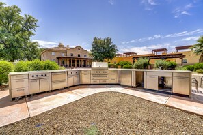 A patio with a built-in kitchen area, a pergola, and a house in the background.