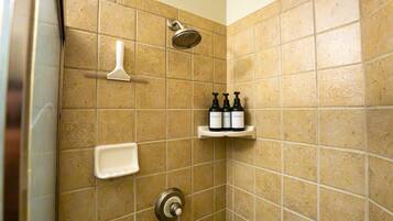 A shower area with a handheld showerhead, a handheld soap dispenser, and a shelf with three bottles of toiletries.