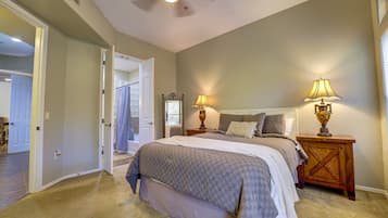 A bedroom with a large bed, two bedside lamps, a ceiling fan, and a view of the bathroom through an open door.