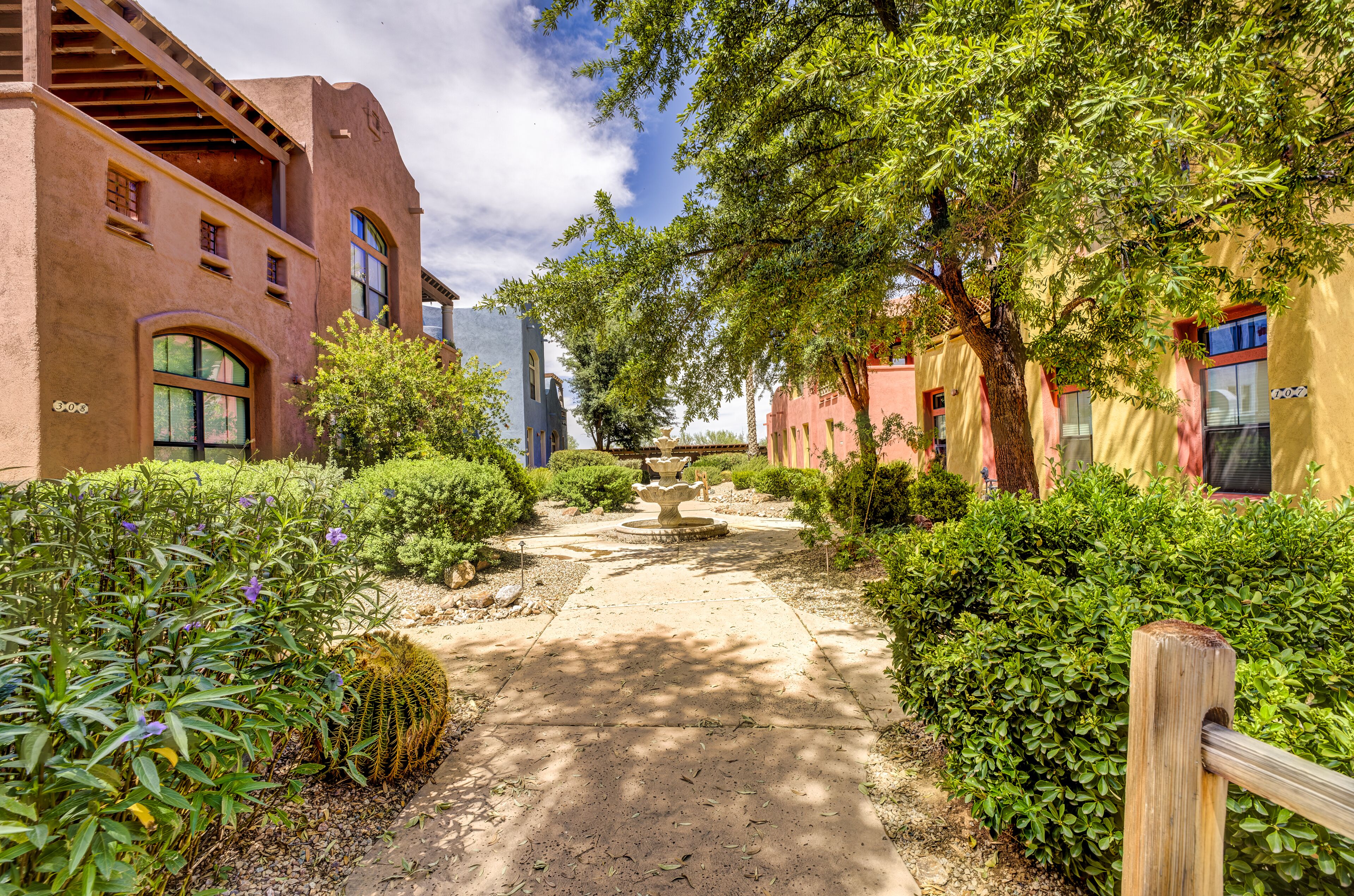 A pathway flanked by buildings with arched windows and a garden with a central fountain.
