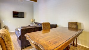 Een eetgedeelte met een houten tafel en stoelen, een bank, een televisie en een plafondventilator.