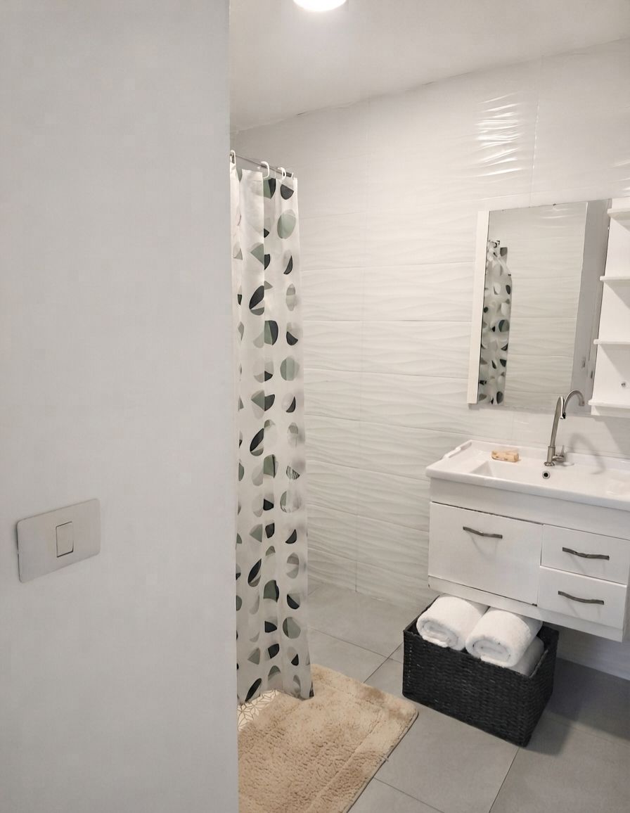 A modern bathroom with a shower curtain, a sink with a mirror, and a towel basket.
