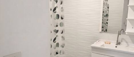 A modern bathroom with a shower curtain, a sink with a mirror, and a towel basket.