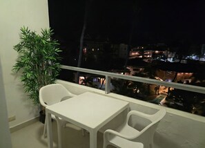 A balcony with a table and chairs, a potted plant, and a view of buildings at night. - Corales Ducassi Rooftop pool & tropical Caribbean sun (Punta Cana)