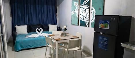 A compact room with a bed, a dining table, and a refrigerator.
