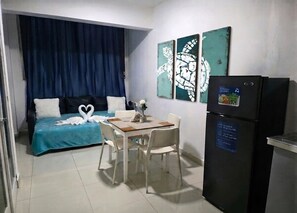 Ein kleines Zimmer mit einem Bett, einem Esstisch und einem Kühlschrank.