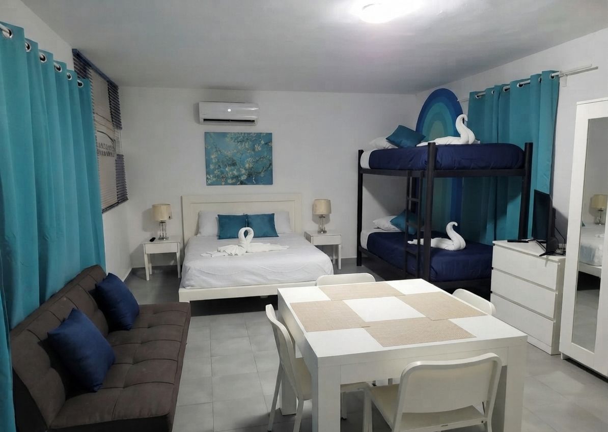 A hotel room with a bunk bed, a sofa, a dining table, and a desk.