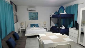 A hotel room with a bunk bed, a sofa, a dining table, and a desk.