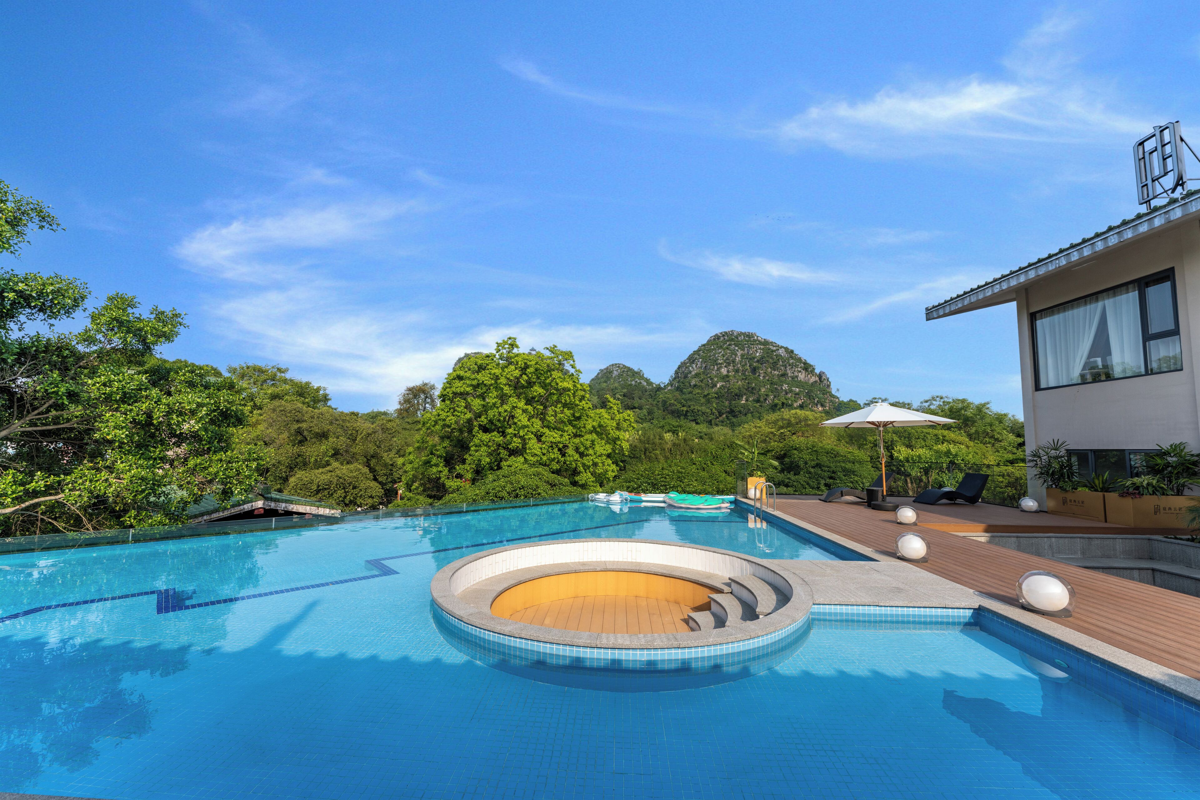 Una piscina con zona de deck de madera, rodeada de exuberante vegetación y una montaña al fondo.