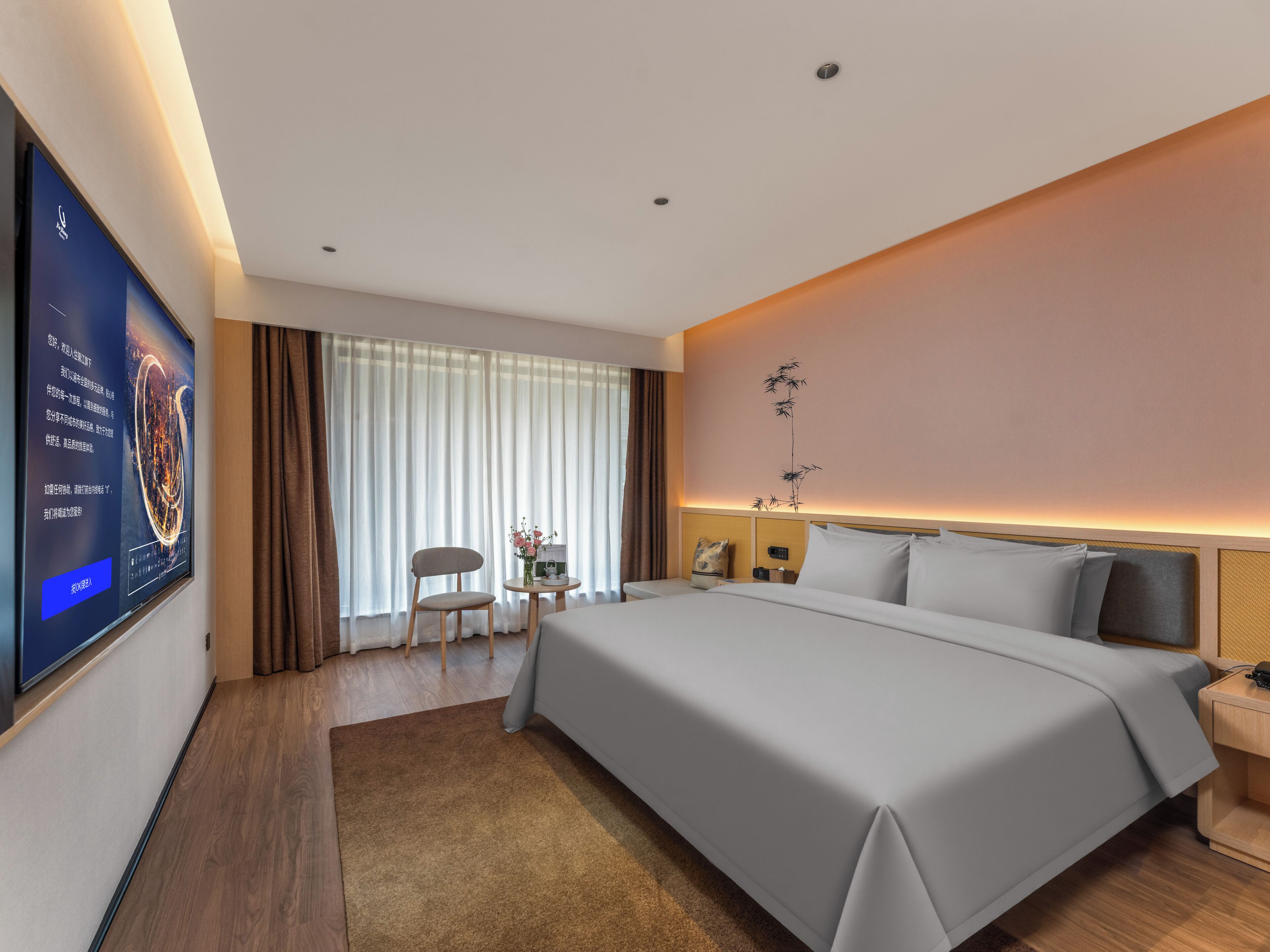 A hotel room with a large bed, a flat-screen TV mounted on the wall, a small table with a vase of flowers, and a chair.