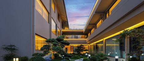 A modern building with a central courtyard, featuring a stone pathway, well-maintained greenery, and a clear sky.
