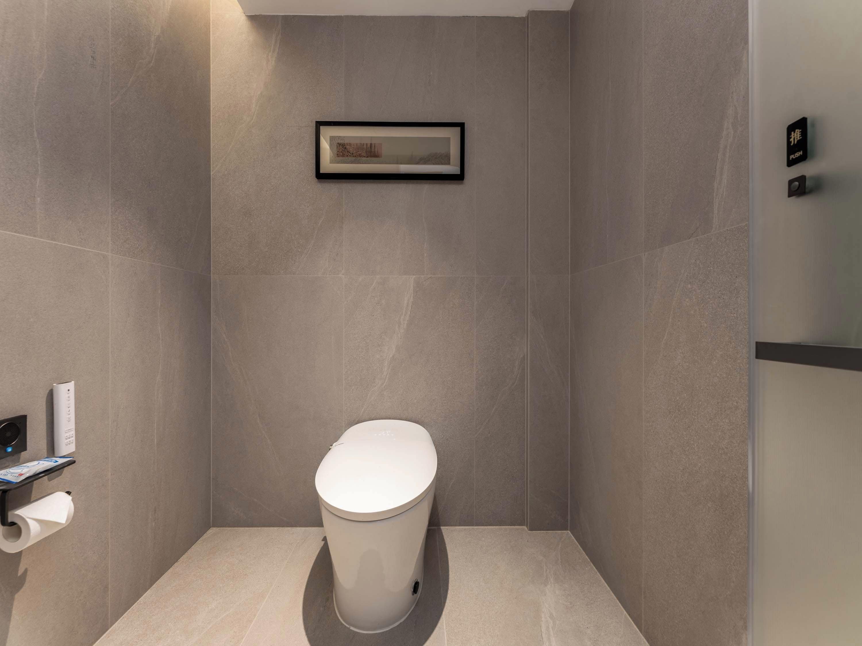 A modern bathroom with a toilet, a framed picture on the wall, and a toilet paper holder.