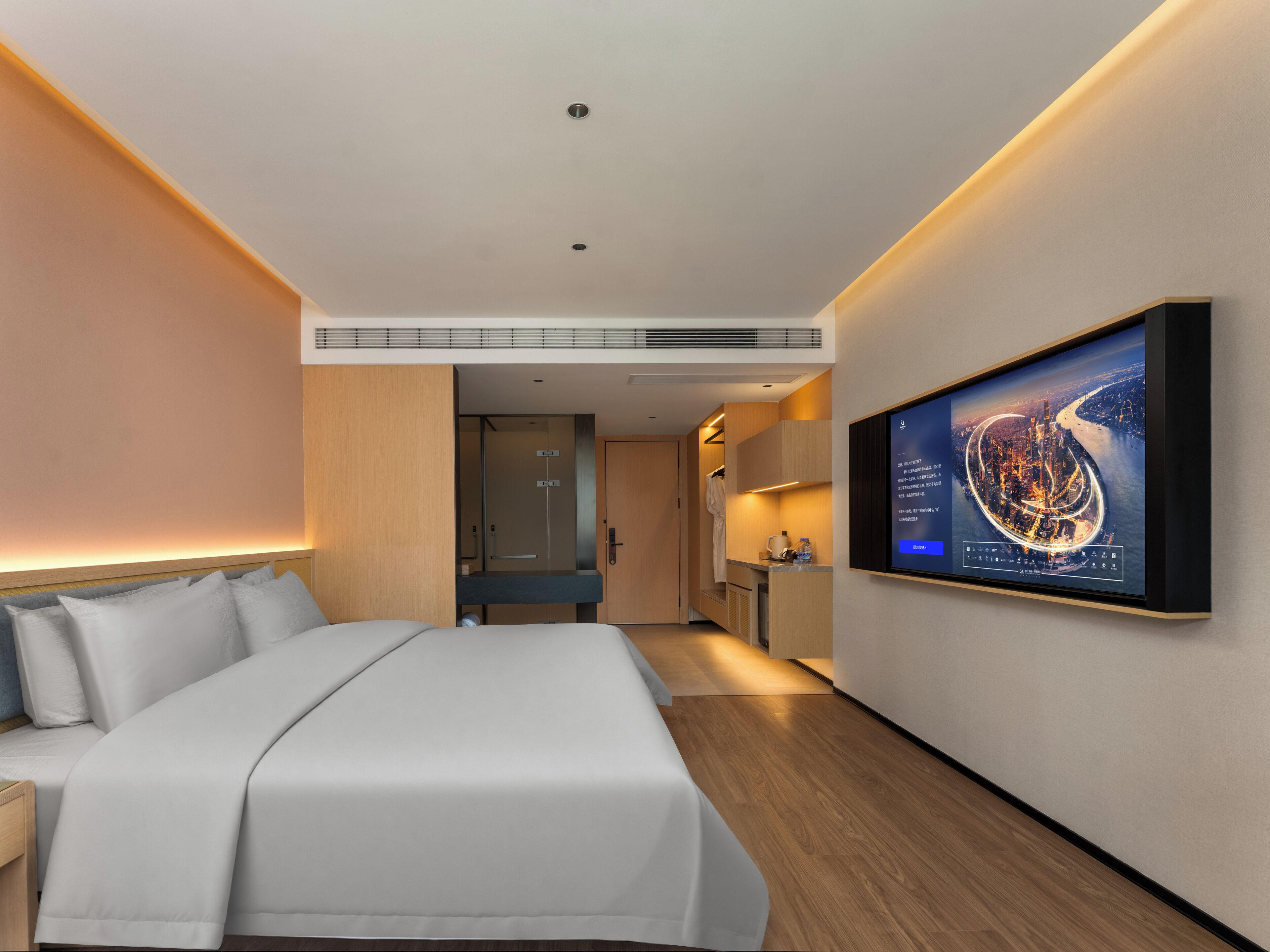 A modern hotel room with a large bed, a flat-screen TV mounted on the wall, and a view of a cityscape.