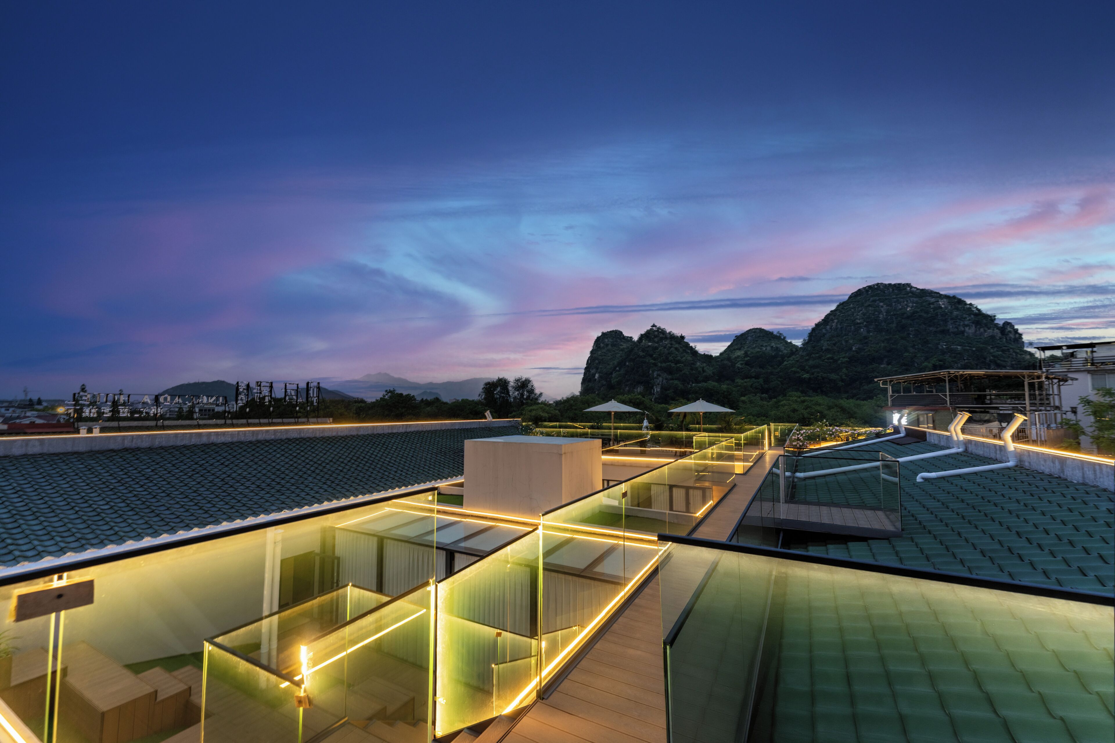 A modern rooftop terrace with glass railings and a view of a mountainous landscape.