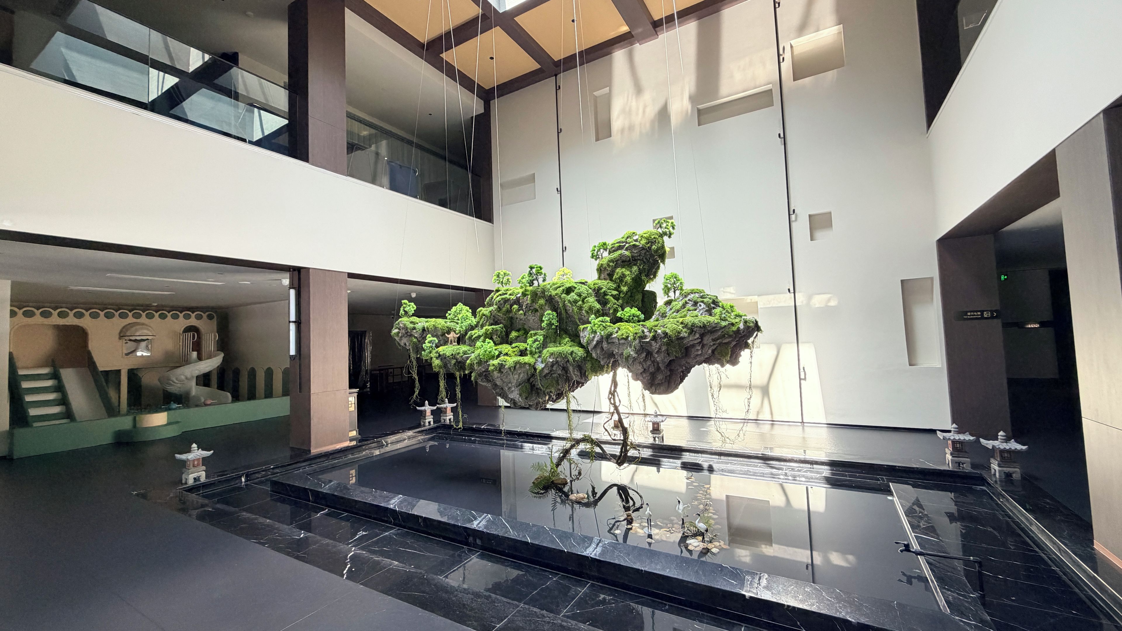Un espacio interior moderno con una fuente de agua reflectante, un jardín vertical de rocas y elementos arquitectónicos tradicionales.