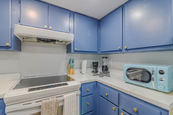 Una cocina con gabinetes azules, una encimera blanca, una estufa, un microondas y una cafetera.