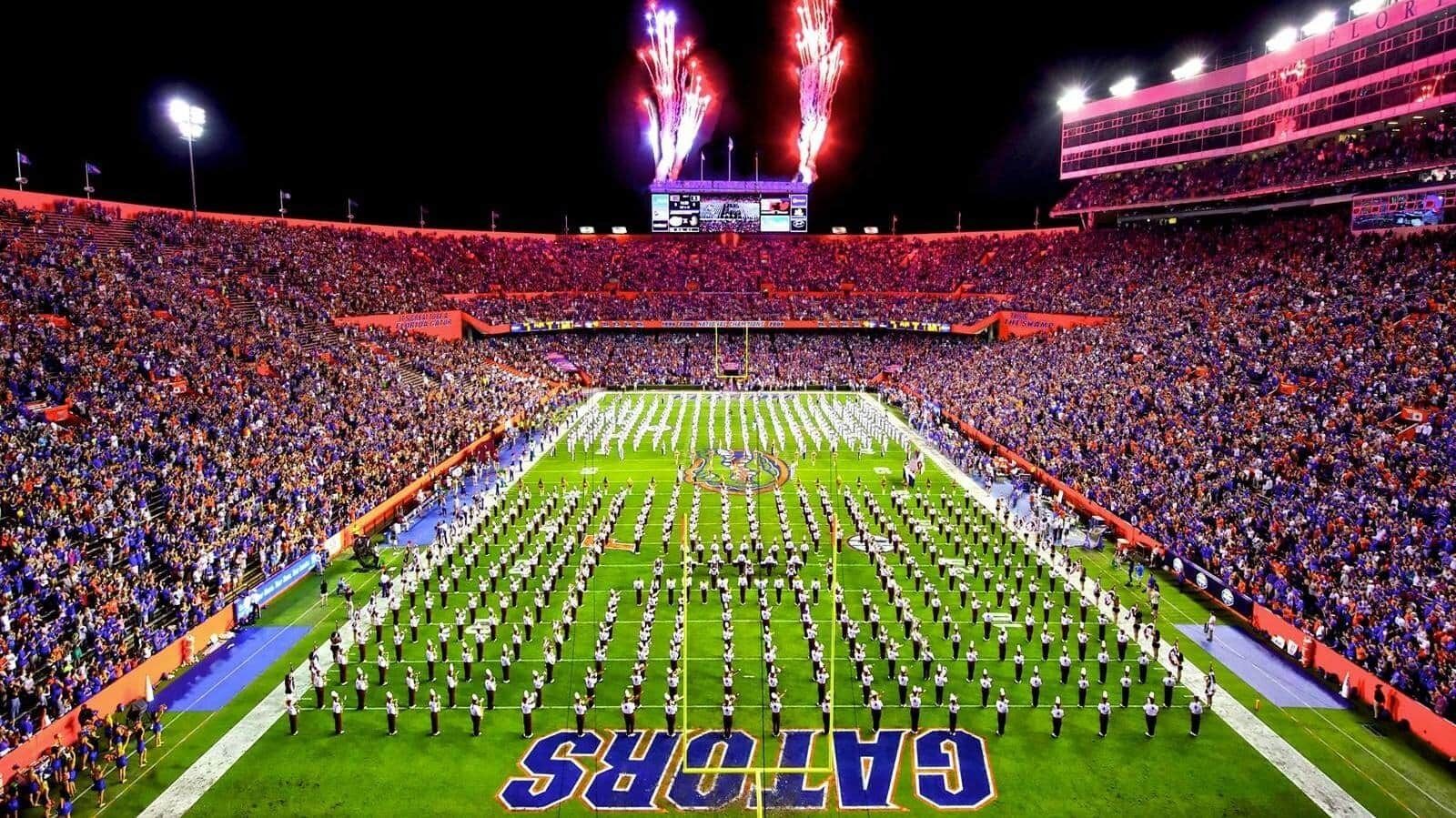 A stadium with a marching band formation on the field, surrounded by a large crowd.