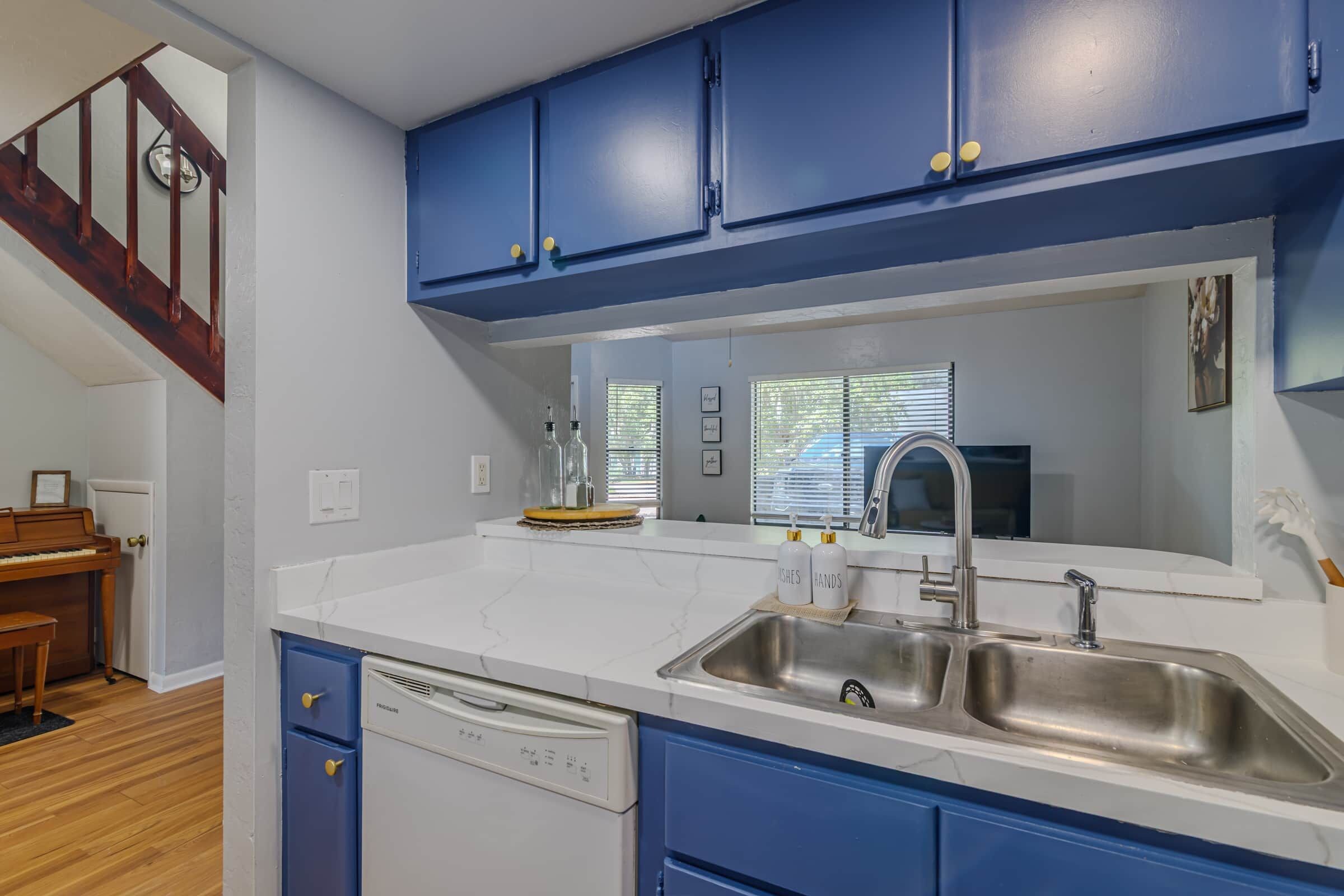 A kitchen with blue cabinets, a white countertop, a stainless steel sink, and a dishwasher.