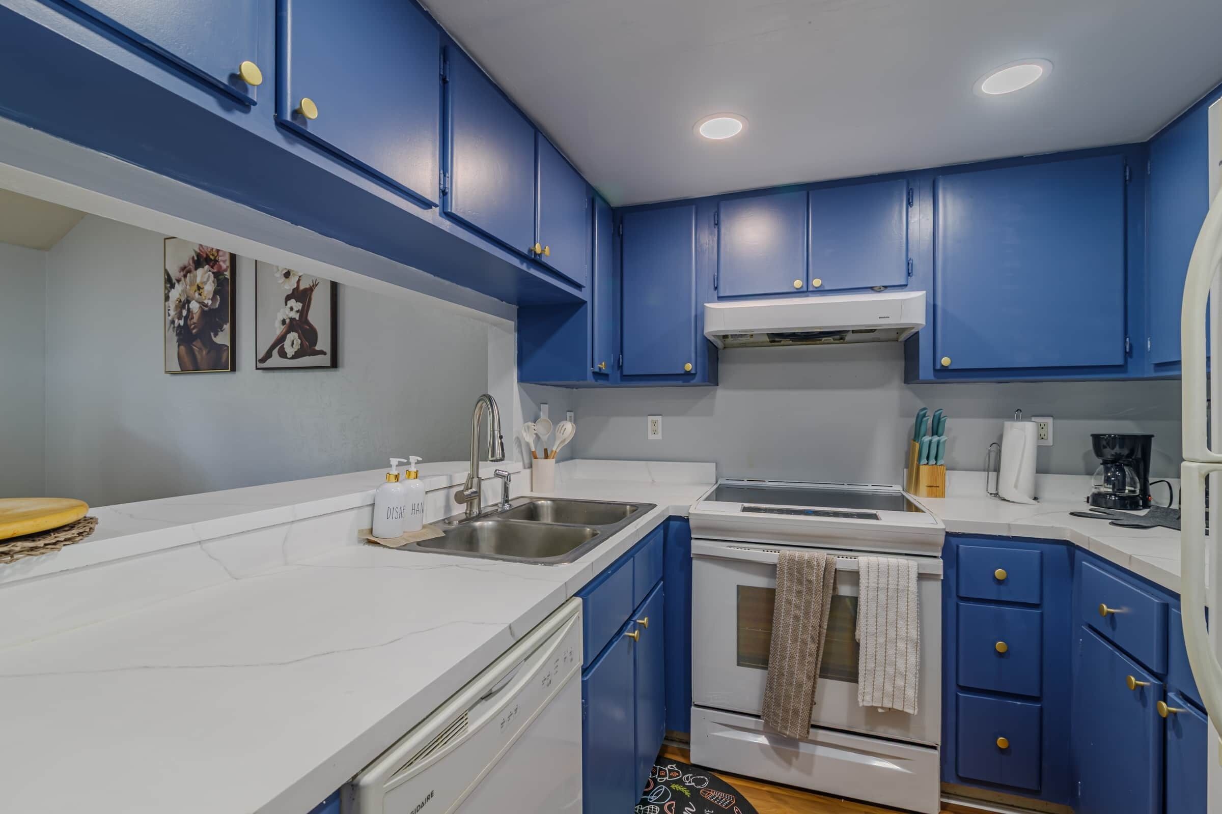 A kitchen with blue cabinets, a white countertop, a sink, a stove, and a coffee maker.